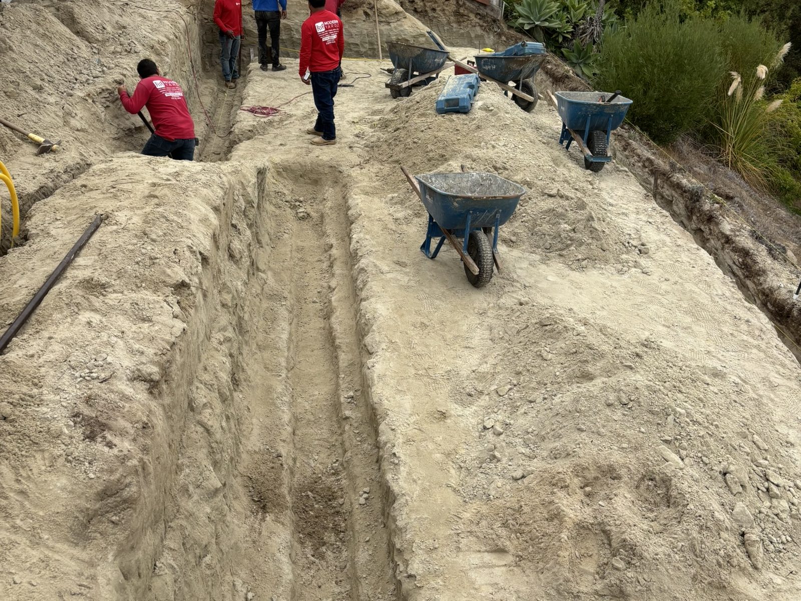 Abshire Brothers Lawn & Landscape crew excavating footing trenches on a sloped Rayne backyard